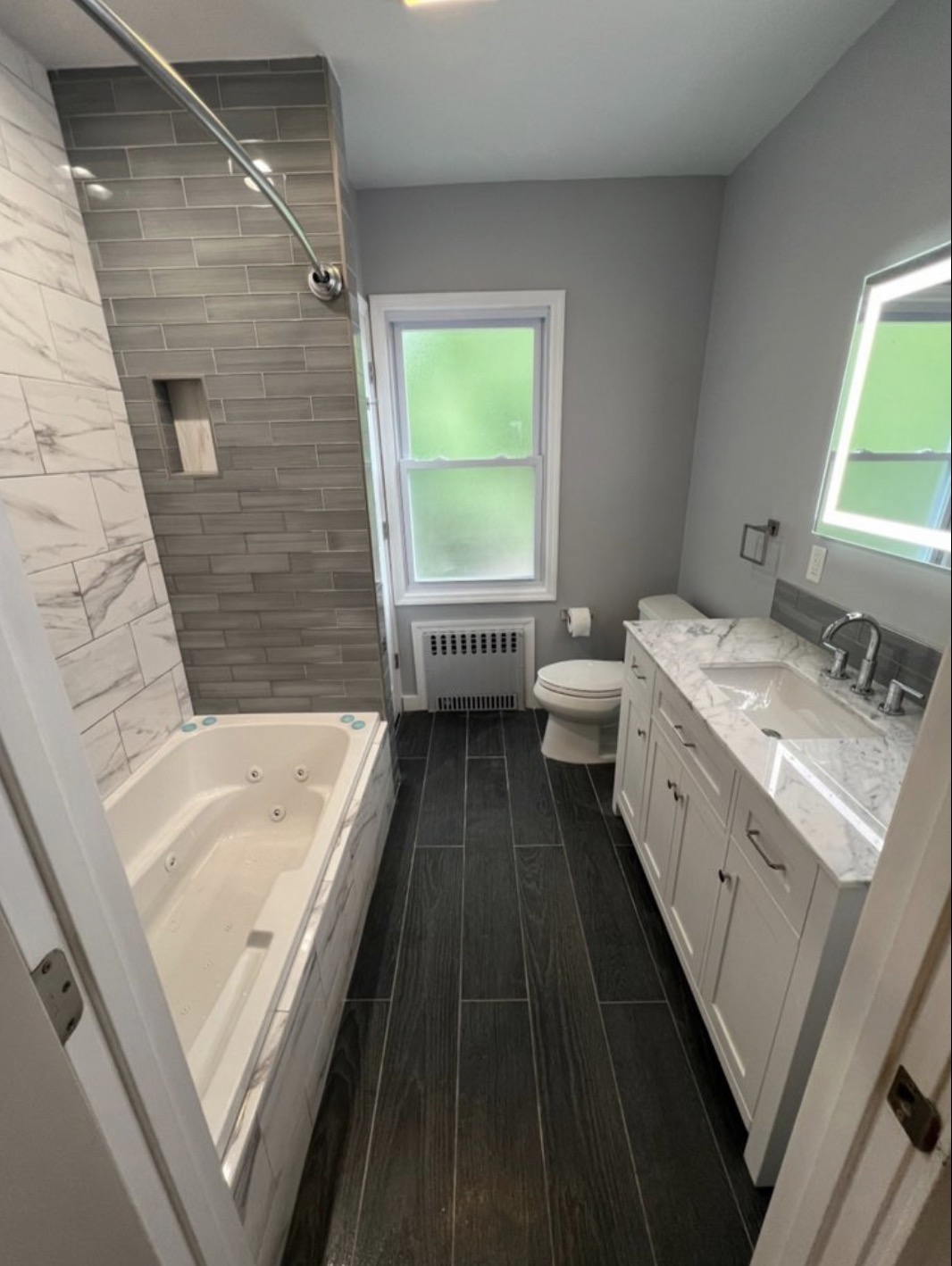 Bathroom renovation with jetted tub, marble tile surround and white vanity
