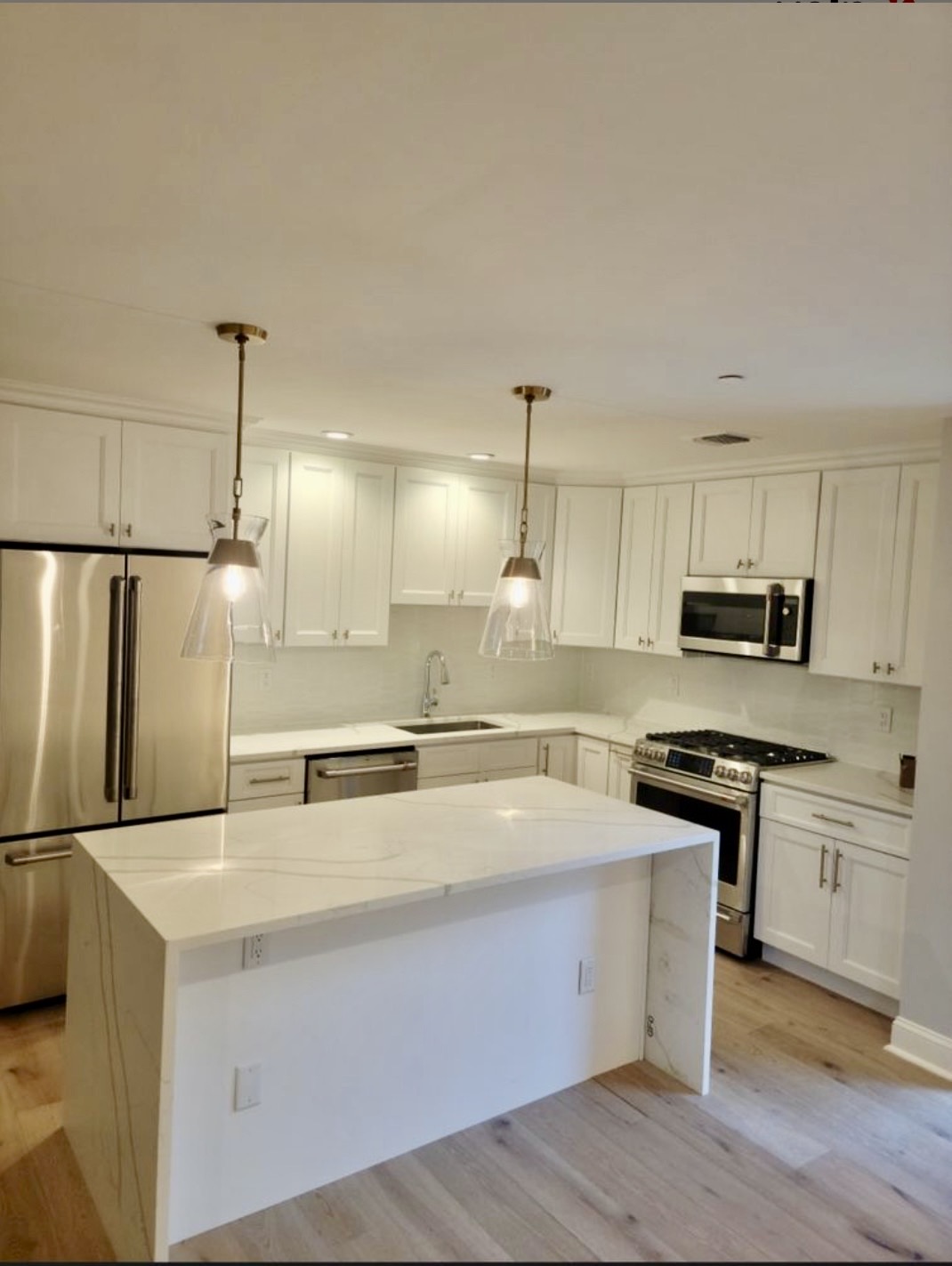 White kitchen with waterfall quartz island and brass pendant lighting